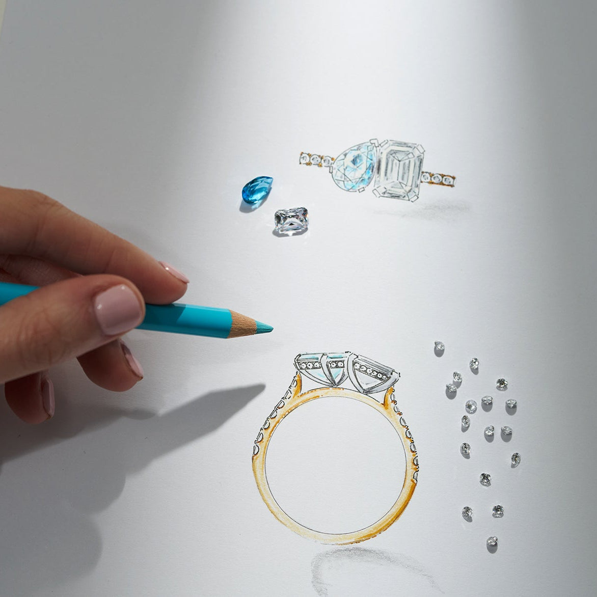 Hand drawing a diamond ring with a blue pencil on white paper.